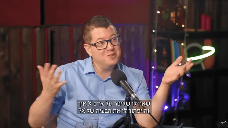 דני אורבך מדבר ומחווה בידיו מול מיקרופון בפודקאסט 'התיקון'